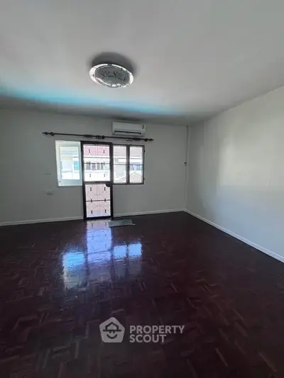 Spacious empty room with wooden flooring and large window, perfect for customization.