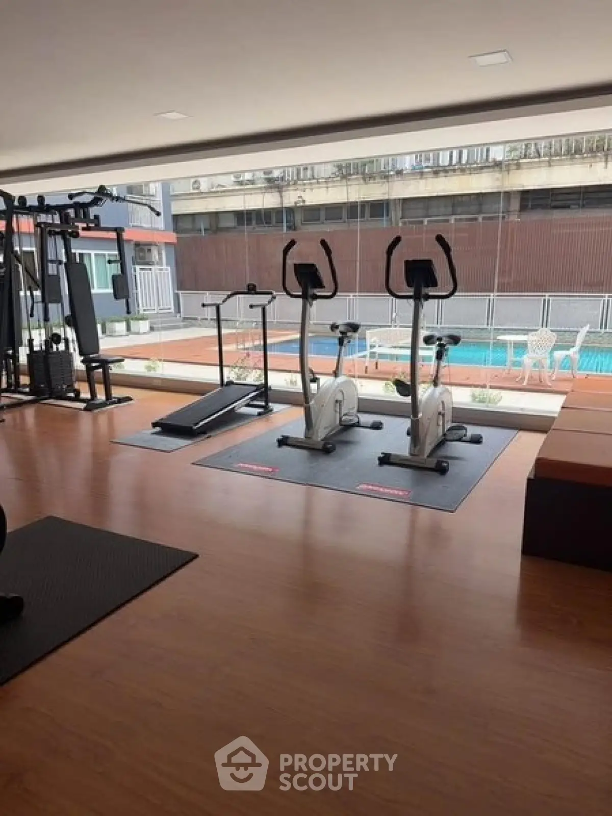 Modern gym with exercise equipment overlooking a pool in a luxury apartment complex.