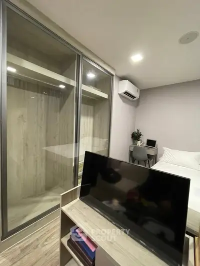 Modern bedroom with sleek closet and workspace, featuring a mounted TV and air conditioning.