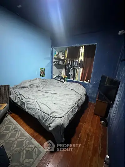 Cozy bedroom with wooden flooring and blue walls, featuring a bed and a small TV for a comfortable living space.