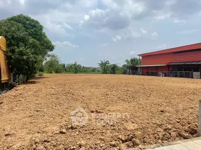 Expansive plot of land with potential for development, adjacent to a modern building and lush greenery.