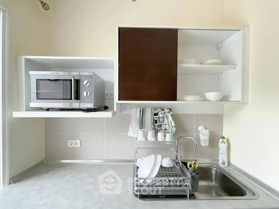 Modern kitchen with microwave, sink, and dish rack in compact layout.