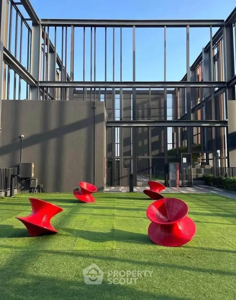 Modern building exterior with unique red outdoor seating on green lawn.