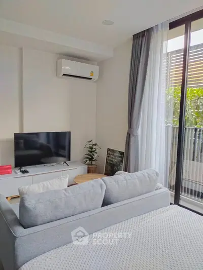 Cozy and modern living room with plush sofa, flat-screen TV, and abundant natural light streaming in from the sliding glass door leading to a refreshing balcony.