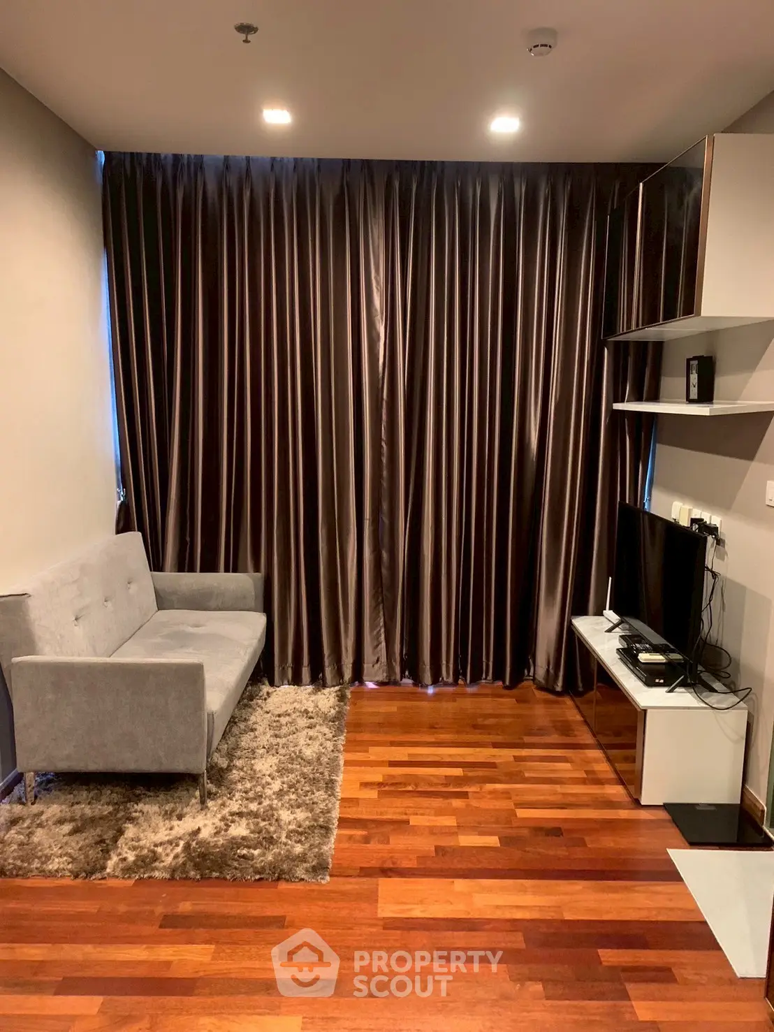Cozy living room with wooden flooring, gray sofa, and entertainment unit, ideal for relaxation.
