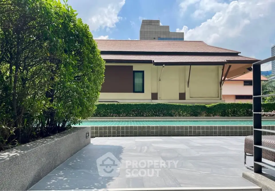 Luxurious poolside view with lush greenery and modern architecture under a clear blue sky.