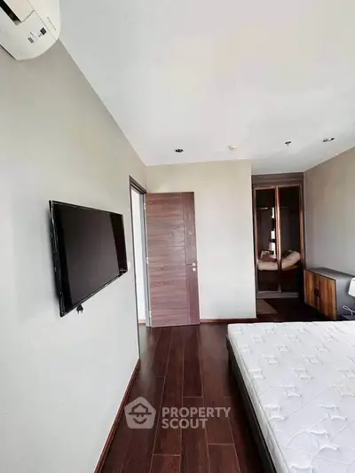 Modern bedroom with wooden flooring and wall-mounted TV in a stylish apartment.