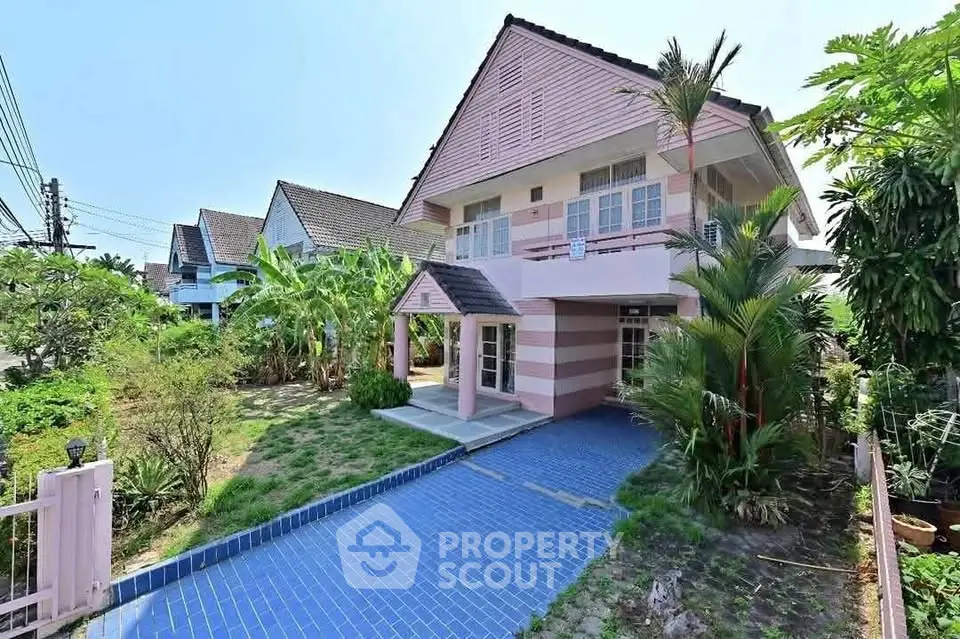 Charming two-story pink house with lush garden and blue-tiled pathway