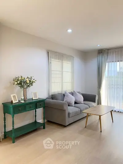 Charming living room with cozy gray sofa, elegant green console table, and natural light from large windows.