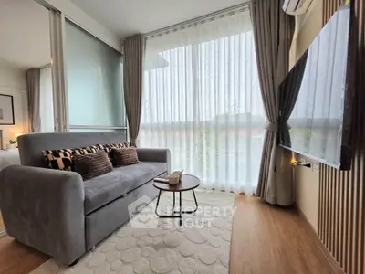Modern living room with cozy sofa, stylish decor, and large window with sheer curtains.