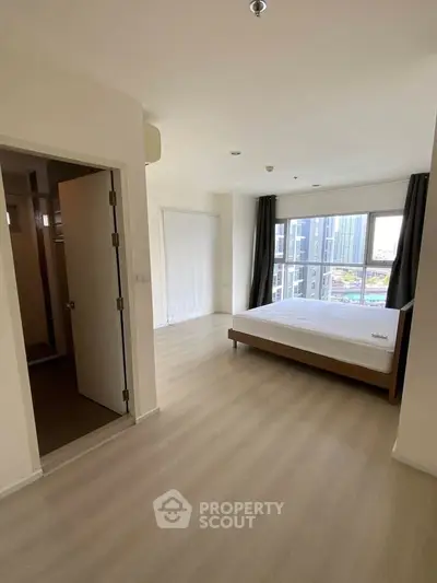 Spacious bedroom with large window offering city views, featuring minimalist decor and natural light.