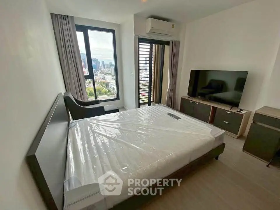 Modern bedroom with city view, featuring a large window, sleek furniture, and a wall-mounted TV.