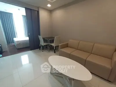 Modern living room with beige sofa, white coffee table, and dining area in open layout apartment.