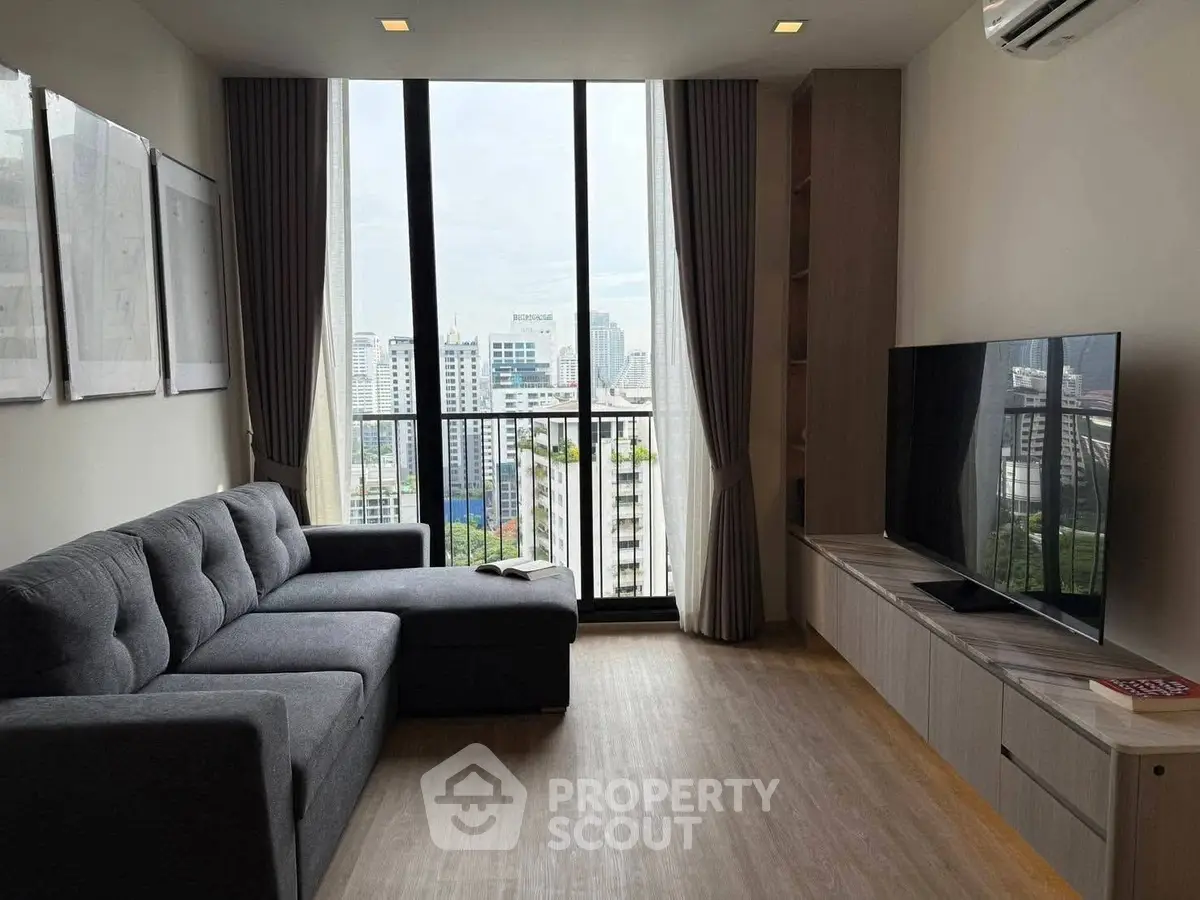 Modern living room with large window and city view, featuring a comfortable sofa and flat-screen TV.