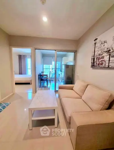Modern living room with beige sofa and marble coffee table, open layout to dining area and bedroom.