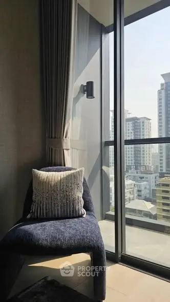 Modern high-rise apartment with city view from balcony, featuring elegant chair and floor-to-ceiling windows.