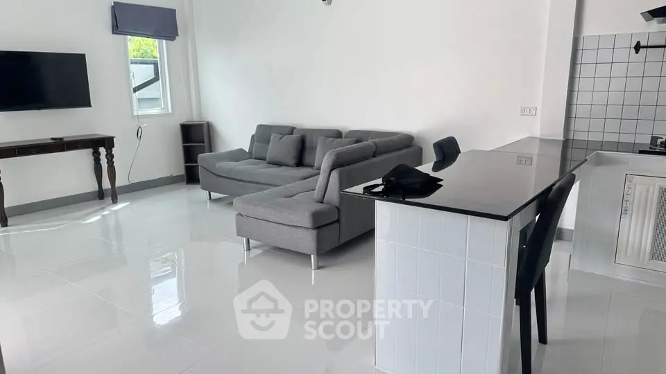 Modern living room with sleek gray sofa and stylish kitchen counter in open layout.