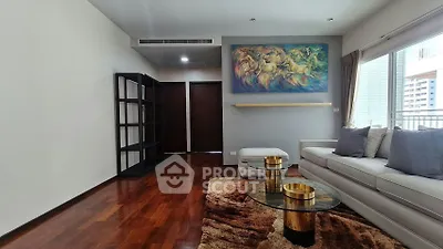 Spacious living room with modern decor and vibrant artwork, featuring hardwood floors and large windows.