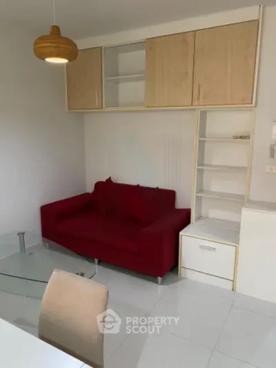 Modern living room with red sofa, glass coffee table, and built-in wooden shelves.