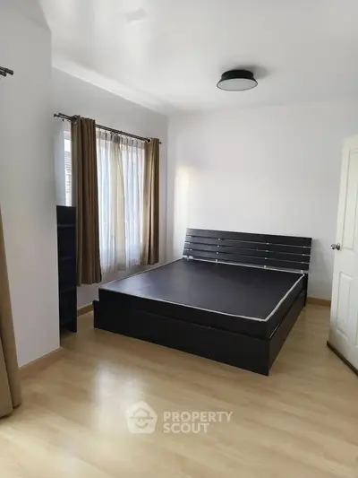 Spacious bedroom with modern black bed frame and natural light from window.