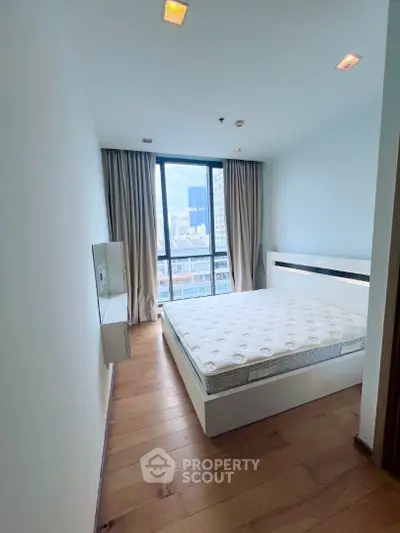 Modern bedroom with large window offering city view, featuring a comfortable bed and wooden flooring.