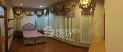 Spacious bedroom with elegant drapes and wooden flooring, featuring a cozy single bed and ample natural light.