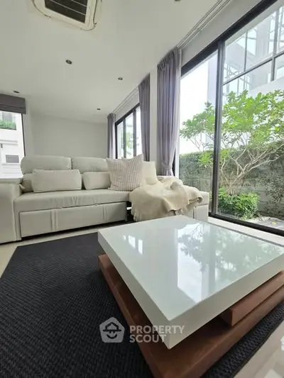 Modern living room with large windows and stylish furniture, offering a serene garden view.