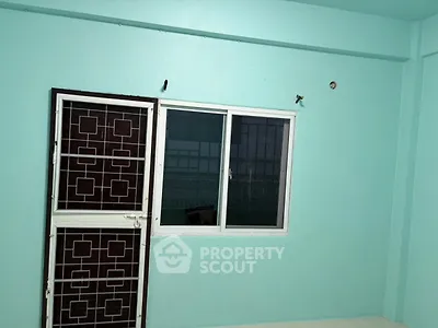 Minimalist room with teal walls and a window with security bars.