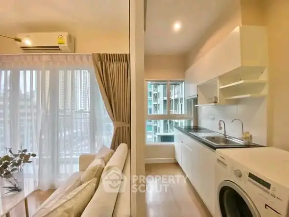 Modern apartment with open kitchen and cozy living area, featuring large windows and natural light.
