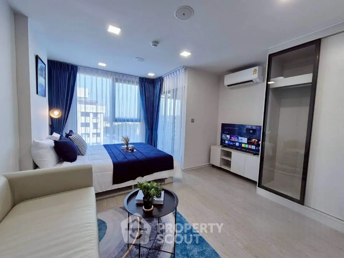 Modern studio apartment with stylish decor, featuring a cozy bed, sleek sofa, and a wall-mounted TV.