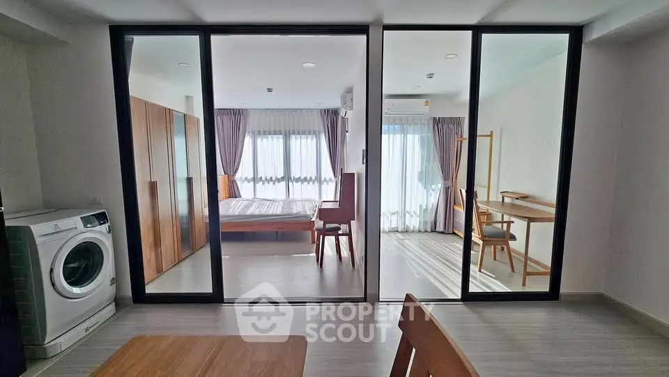 Modern apartment interior with glass partition, featuring bedroom and study area, washing machine included.