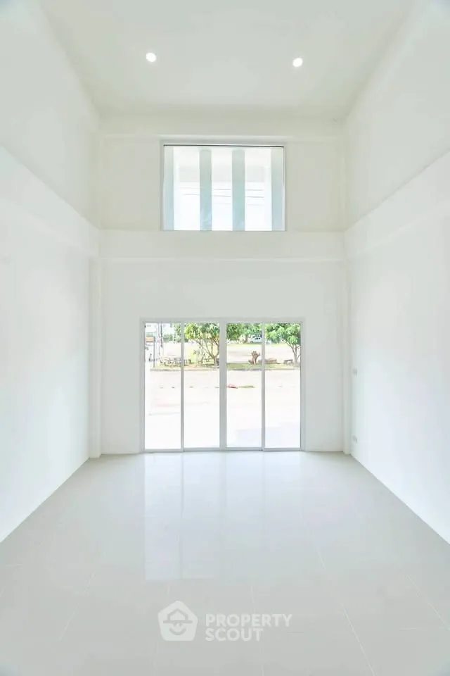 Spacious white-walled room with high ceiling and large windows offering natural light.