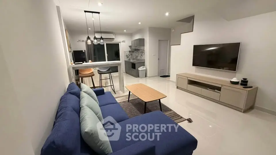 Modern living room with open kitchen, blue sofa, and wall-mounted TV in a stylish apartment.