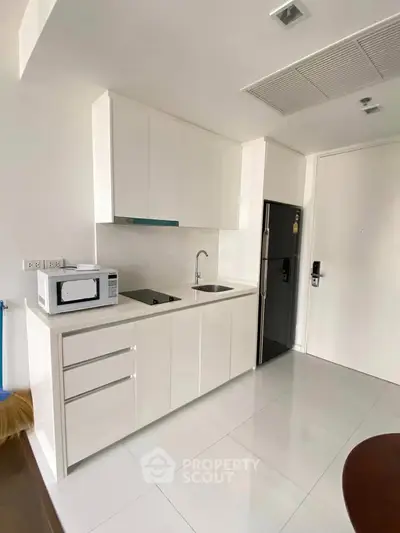 Modern compact kitchen with sleek white cabinetry and built-in appliances in a stylish apartment.