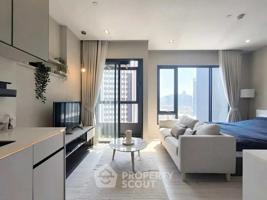 Modern open-plan living room with kitchen and city view, featuring sleek furniture and natural light.
