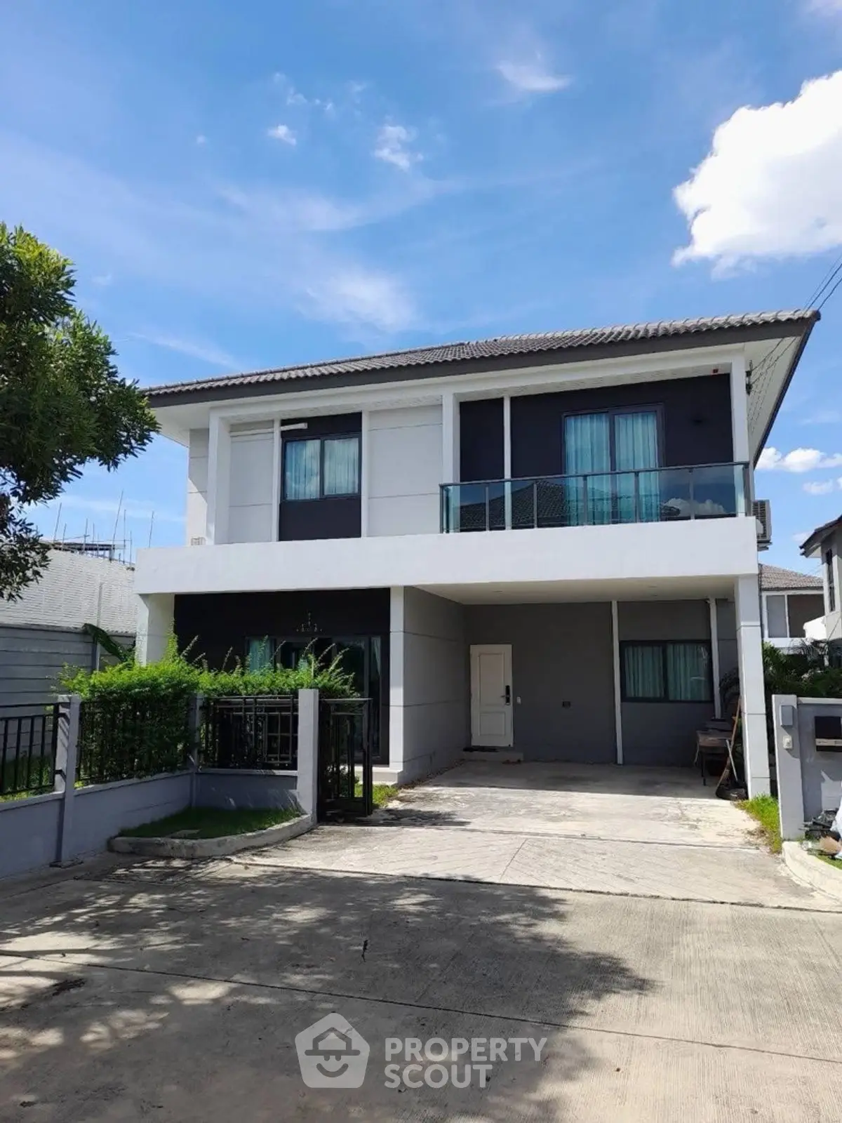 Modern two-story house with spacious driveway and lush greenery under a clear blue sky.