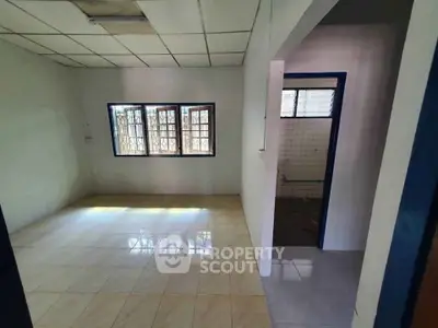 Spacious empty room with tiled floor and large windows in a well-lit interior space.