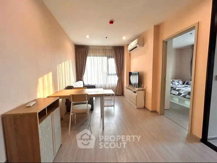 Modern living room with dining area and view into bedroom, featuring sleek furniture and natural light.
