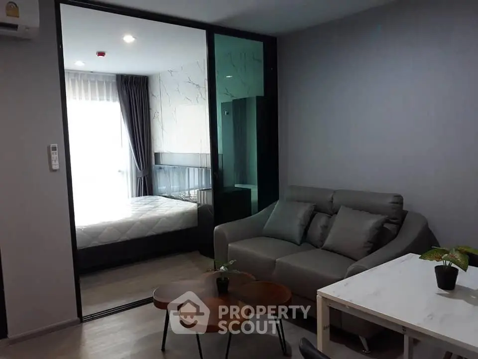 Modern living room with cozy sofa and stylish decor adjacent to a bedroom with glass partition.