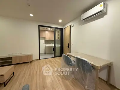Modern apartment interior with open kitchen and dining area, featuring wood flooring and air conditioning.