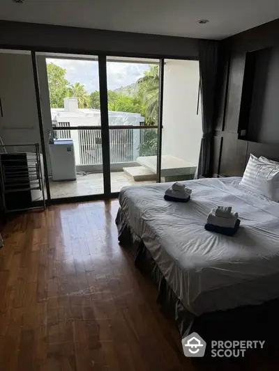 Spacious bedroom with balcony and scenic view, featuring modern decor and wooden flooring.