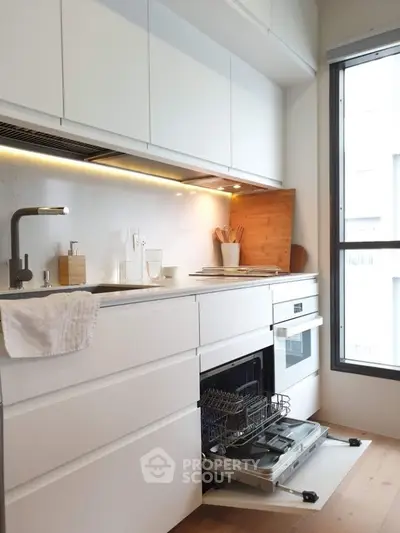 Modern kitchen with sleek white cabinetry and built-in appliances, featuring a dishwasher and large window.