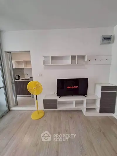 Modern living room with sleek TV stand and open kitchen layout, featuring a bright yellow fan for a pop of color.