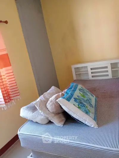 Cozy bedroom with striped mattress and colorful pillows, perfect for relaxation.