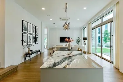 Luxurious open-plan living room with elegant dining area and large windows overlooking greenery.