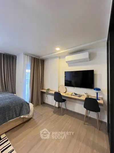 Modern bedroom with wall-mounted TV and workspace, featuring stylish decor and natural light.