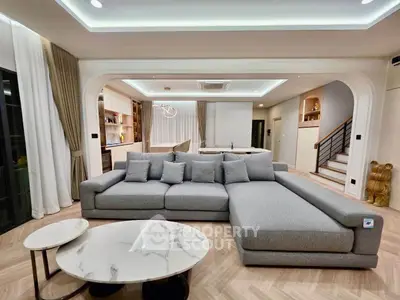 Spacious modern living room with elegant gray sectional sofa and marble coffee tables, open to a stylish kitchen.