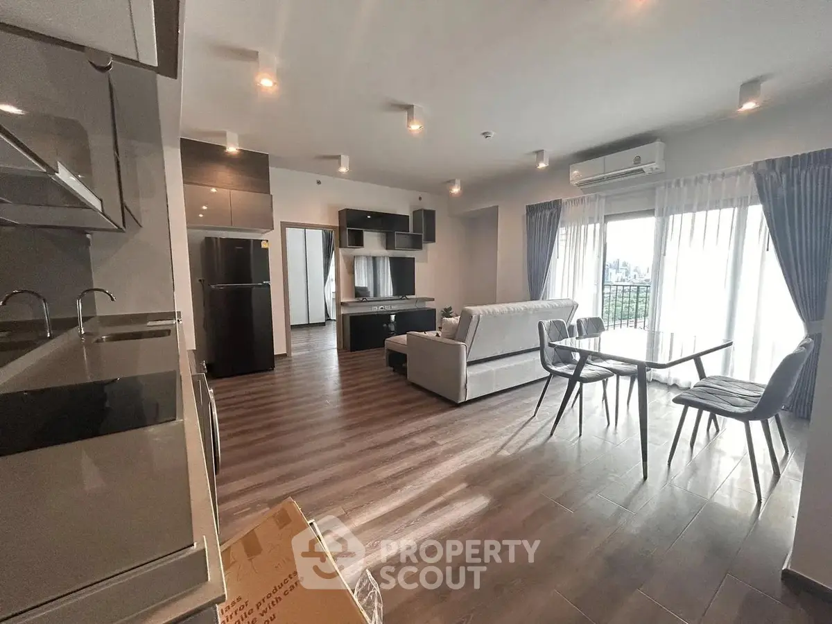 Spacious modern living room with open kitchen and balcony view, featuring sleek furniture and ample natural light.