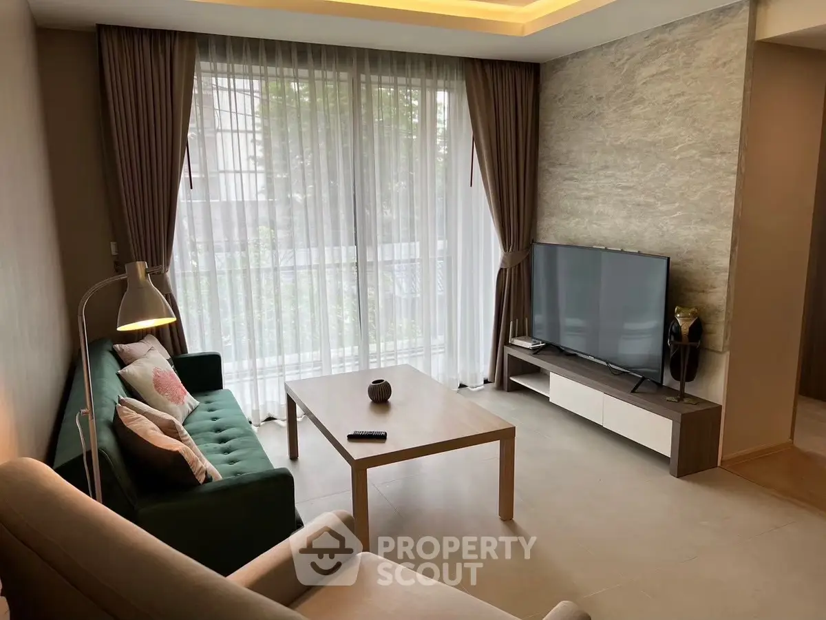 Modern living room with stylish furniture and large TV, featuring floor-to-ceiling windows and elegant curtains.