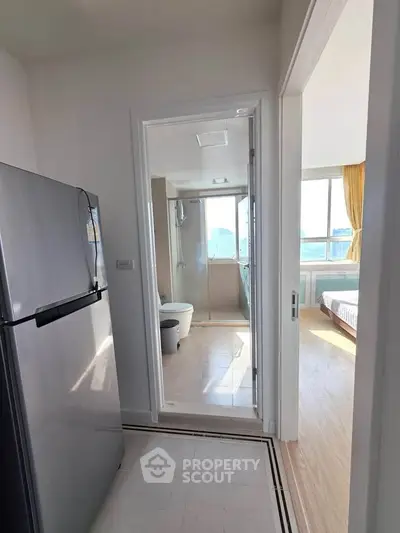 Modern apartment interior with kitchen and bathroom view, featuring natural light and sleek design.